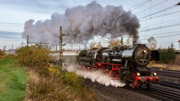 Das Bild zeigt die Dampflok 52 8154 des Eisenbahnmuseums Leipzig mit ausgeprägter Dampffahne, welche sich über den Zug legt. Die Lanschaft ist herbstlich.